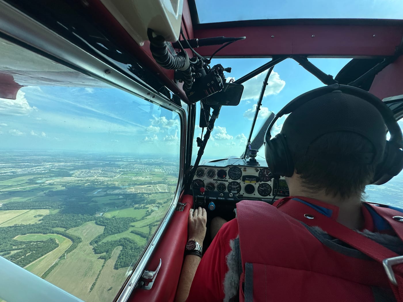 Pilot at the controls in flight over Dallas–Fort Worth farmland, seen from the back seat
