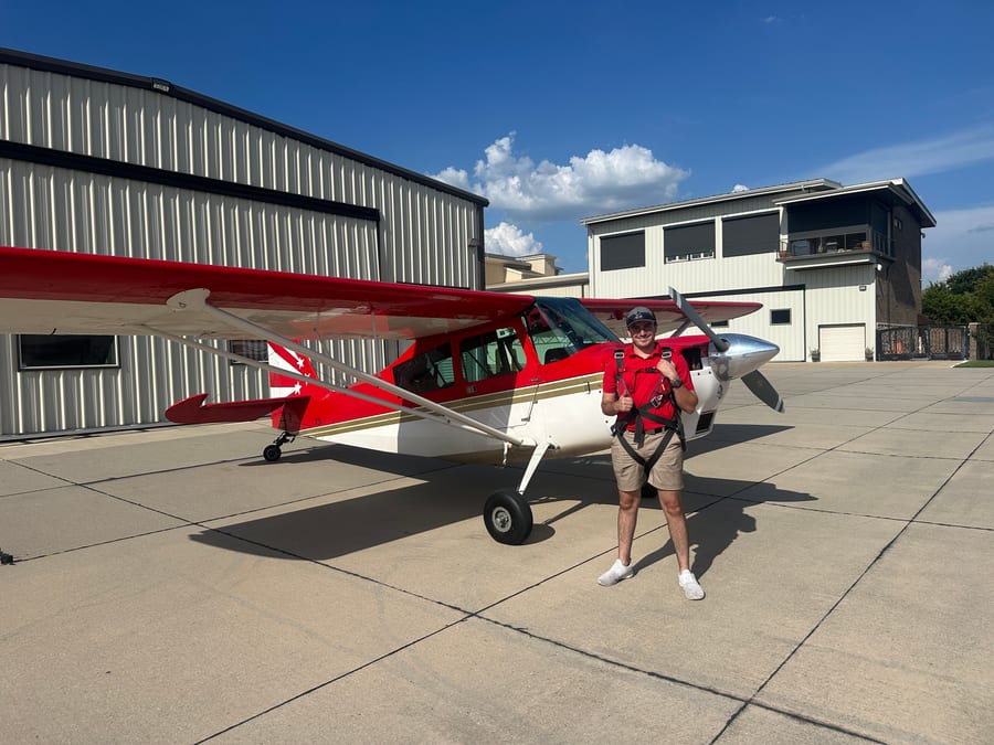 Reid Pekowski standing beside a red and white tailwheel airplane on the ramp